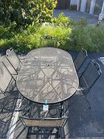 Top-down view of oval wrought iron patio table surrounded by six matching chairs, showing mesh surface and umbrella hole in table center.