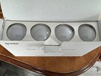 Open box showing four white frosted glass A19 smart light bulbs with silver screw bases inside a white insert.