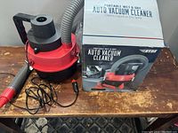 Photo showing the portable wet and dry auto vacuum cleaner unit with attached hose, power cord with car plug, nozzle attachment, and original packaging box.