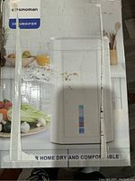 Front of box showing white Cosmoman dehumidifier with water level indicator and food items in background, box is damaged