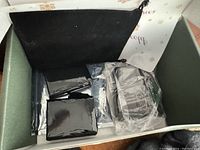 Green storage box with black interior containing packaged batteries and charger wrapped in plastic.
