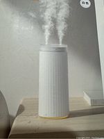 White cylindrical humidifier on wooden surface with mist emitting from top, showing nightlight base glow.