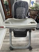 Front view of gray Ingenuity high chair showing padded seat, large attached tray, and sturdy frame.