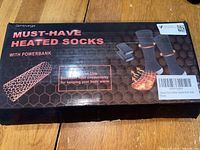 Box showing product name 'Must-Have Heated Socks with Powerbank' and illustration of socks with heating zones and dual powerbank units.