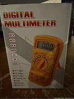 Box of a new digital multimeter showing front view with features listed on the side including DCV, ACV, DCA, HFE, ohm, diode test, and data hold