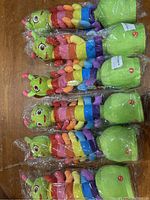 Five identical plush rocking caterpillar toys in plastic, visible colorful striped bodies and green bases.