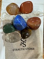 Seven polished stones of different colors on a branded Stealth Stone pouch.
