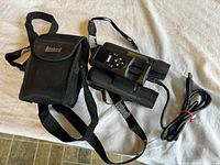 Bushnell binoculars with attached strap, carrying case, and USB cable laid out on a light fabric surface.