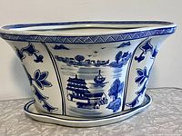 Front view of oval blue and white porcelain planter showing scenic landscape and floral decoration.