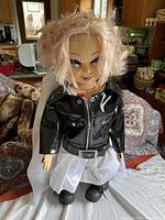 Front view of Tiffany doll standing on a white surface with a background showing a kitchen and furniture.