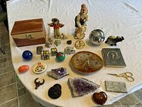 Overview of all items on white tablecloth including wooden box, figurines, crystal ball, clock, various stones and crystals, Rubik's cube and other collectibles.