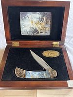 Wooden display case open showing knife and DU logo plaque inside base with wolf print inset on case lid.