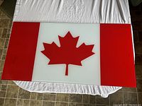 Top view of the rectangular glass panel depicting the Canadian flag on a white cloth background with tile floor visible.