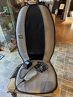 Full view of the Homedics massage cushion showing its back and seat design, remote control with buttons, and power adapter cord.