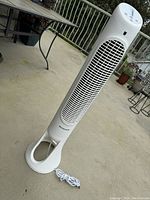 White Honeywell QuietSet Tower Fan shown on an outdoor concrete floor, standing upright with power cord coiled at the base.
