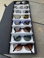 Seven pairs of ladies new sunglasses arranged in a black display case, showcasing a variety of styles and colors.