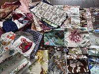 Photo showing assorted vintage and modern fabric pieces with floral, leaf, and other intricate patterns in multiple colors spread on a floor.