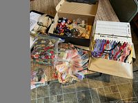 Overview of large assortment of embroidery threads in plastic bags, a box with more supplies, and thread organizer on table.