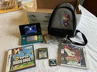 Nintendo 3DS console powered on with home screen, games and carrying case laid out, charger cable present