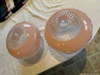 Top view of two round pink and clear glass light shades showing embossed decorative patterns on top and sides.