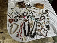 Full assortment of vintage costume jewelry laid on a white cloth showing multiple necklaces, bracelets, brooches, and earrings.
