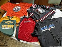 Five sport jerseys and t-shirts laid out on a table showing variety of teams and colors