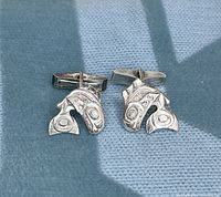 Front view of pair of hand-carved Orca sterling silver cuff links on fabric surface.