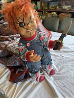 Front view of Chucky doll showing facial details, clothing, and knife held in right hand.