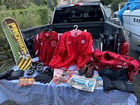Full lot overview on a truck bed showing all items including red Team Canada jacket, Adidas soccer boots, biking shoes, gloves, newspapers, sports bag, knee protectors, and trick board.