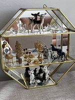 Front view of entire vintage brass mirrored curio cabinet filled with assorted miniatures including crystal animals and porcelain deer figurines on glass shelves