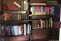 Full view of multiple shelves filled with various hardcover and paperback books including multi-volume encyclopedias and leather-bound editions, with decorative iron bookends visible.