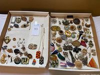 Full view of two boxes containing assortment of brooches, tie clips, and buckles with various animal designs and shapes.