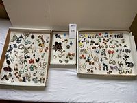 Wide view of 3 trays displaying a large variety of earrings, including dangle, post, and clip-on styles in various colors and shapes.