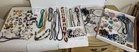 Overview of multiple necklaces, earrings, beads, chains, and jewelry findings laid out on white towels and trays
