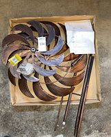 Disassembled metal curved-blade spinner elements and two metal poles lying in a cardboard box with assembly instructions.