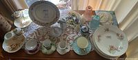 Table display of assorted floral china, doilies, napkin rings, dishes, bowls, tea cups and saucers in natural light
