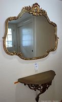 Front view of ornate gilded mirror with detailed carved floral and shell crest and wall-mounted console table below.
