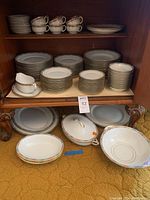 Photo showing stacks of dinnerware plates, cups, saucers and serving bowls in cabinet.