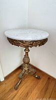 Full view of the round marble-top table showing the grapevine decorative metal base, three legs ending in claw feet, and marble top.
