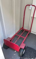 Red Milwaukee 30080 hand truck standing upright against wall, showing handle and base plate with two small caster wheels visible at front.