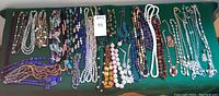 Wide assortment of various beaded and stone necklaces laid flat, showing diversity in length, color and materials.