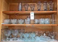 Wood cabinet shelf holding 8 Vetravir old fashioned glasses, stemmed sundae and parfait dishes, float glasses, and small serving bowls with textured patterns.