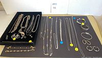 Overview of entire lot on black mat, showing tray of necklaces and earrings at left and assorted chain necklaces, bracelets and earrings on right
