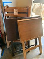 Three wooden TV trays in different wood finishes showing foldable legs and flat surfaces with scratches.