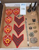 Top down photo showing five FMF-PAC patches, four rank chevrons, metal pins, a bracelet, and two trumpet mouthpieces in a cardboard box.