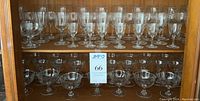 Cabinet shelf with six rows of etched stemware glasses in various sizes and shapes, all matching in etched design, glass and stem style. Approximately 75 pieces total.
