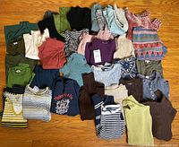Photo showing 35+ pieces women's sweaters and long sleeve tops laid out on floor, various colors and patterns including solids, stripes, and one graphic sweatshirt