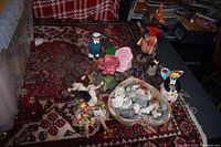 Overview of assorted vintage dolls and figurines arranged around a basket of polished rocks on a patterned rug.