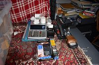 Wide shot of various office supplies arranged on a patterned carpet including calculators, stapler, hole puncher, and tape dispenser.