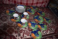 Overview of the lot showing multiple appetizer plates, small white bowls, and white cups with saucers arranged on patterned textile.